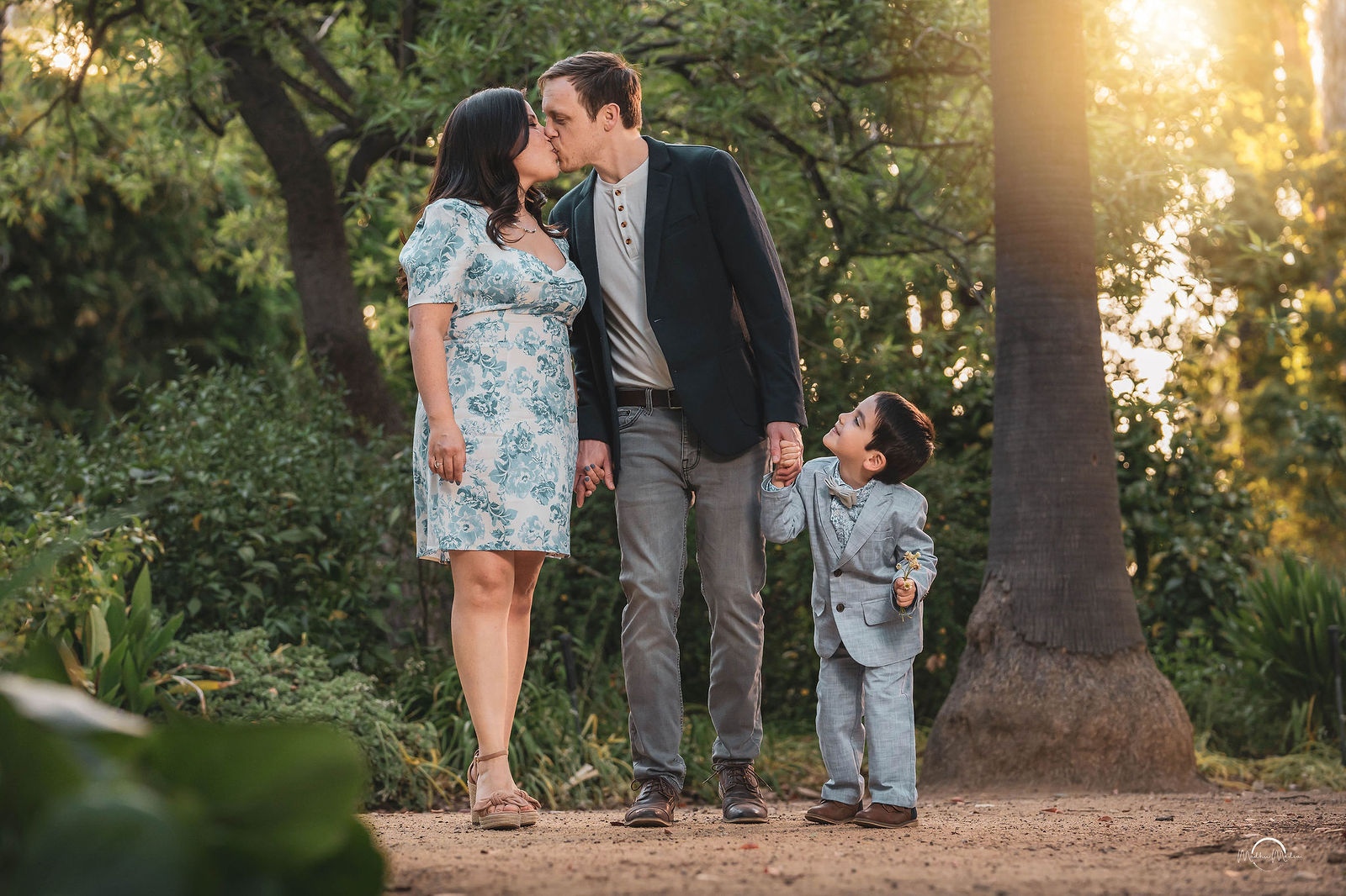 Mom and dad kissing while their son in a little suit looks up