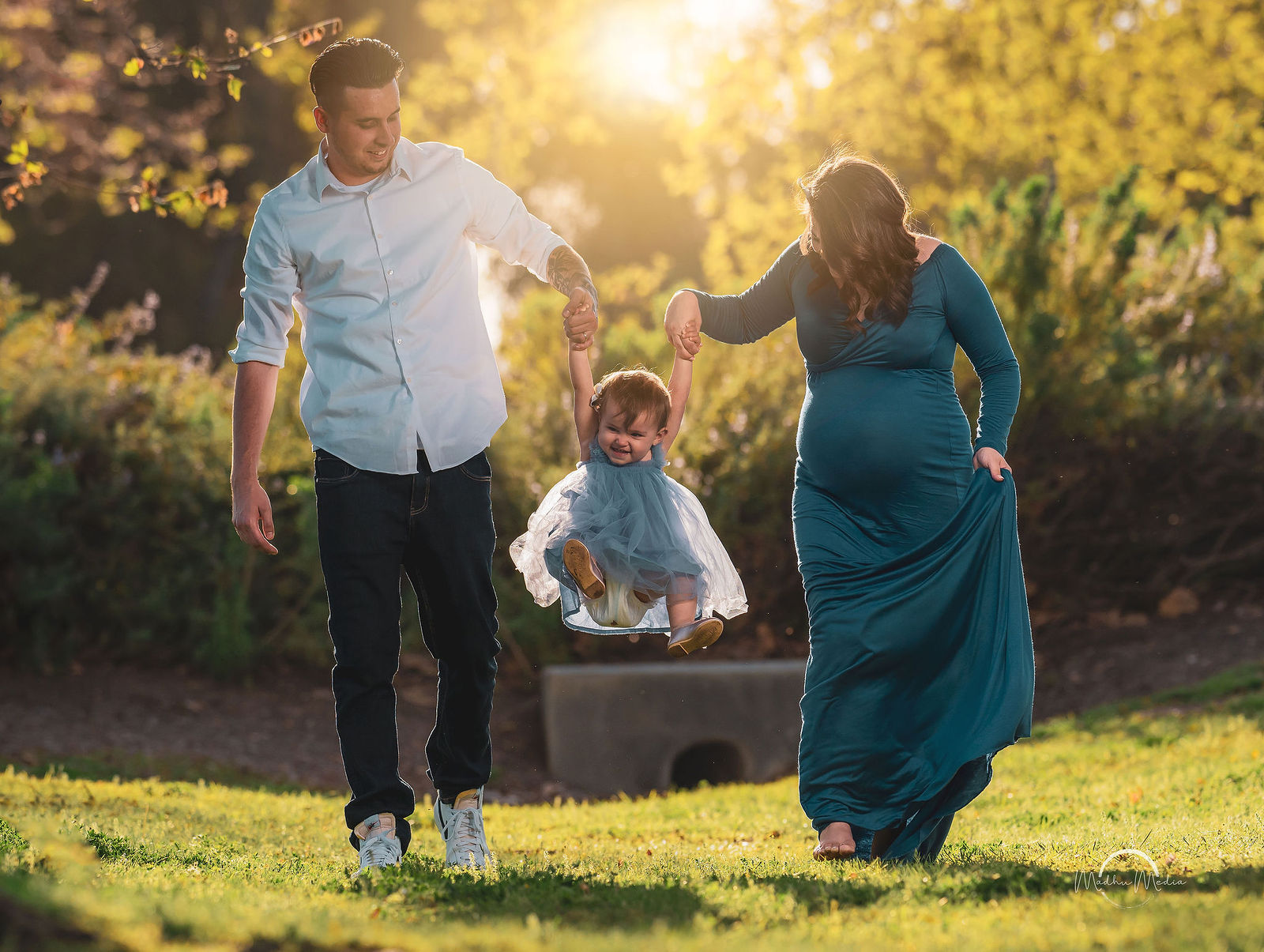 Swinging their daughter through the golden light, baby on the way