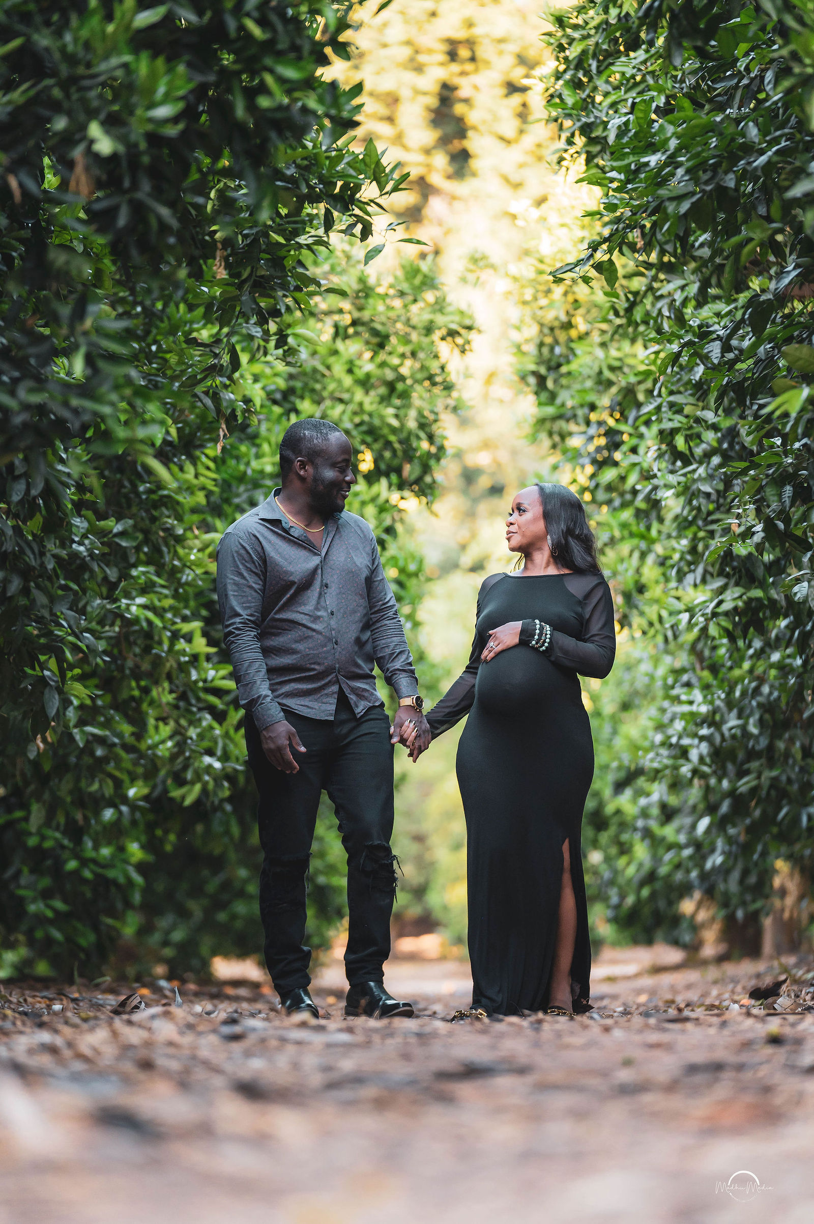 Expecting couple hand in hand on an orchard path