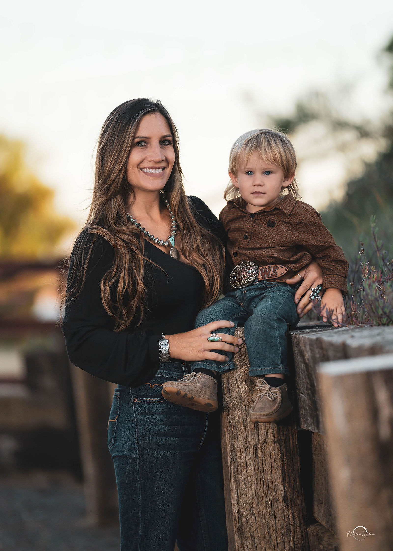 Mom and her boy in western wear up on the ranch fence
