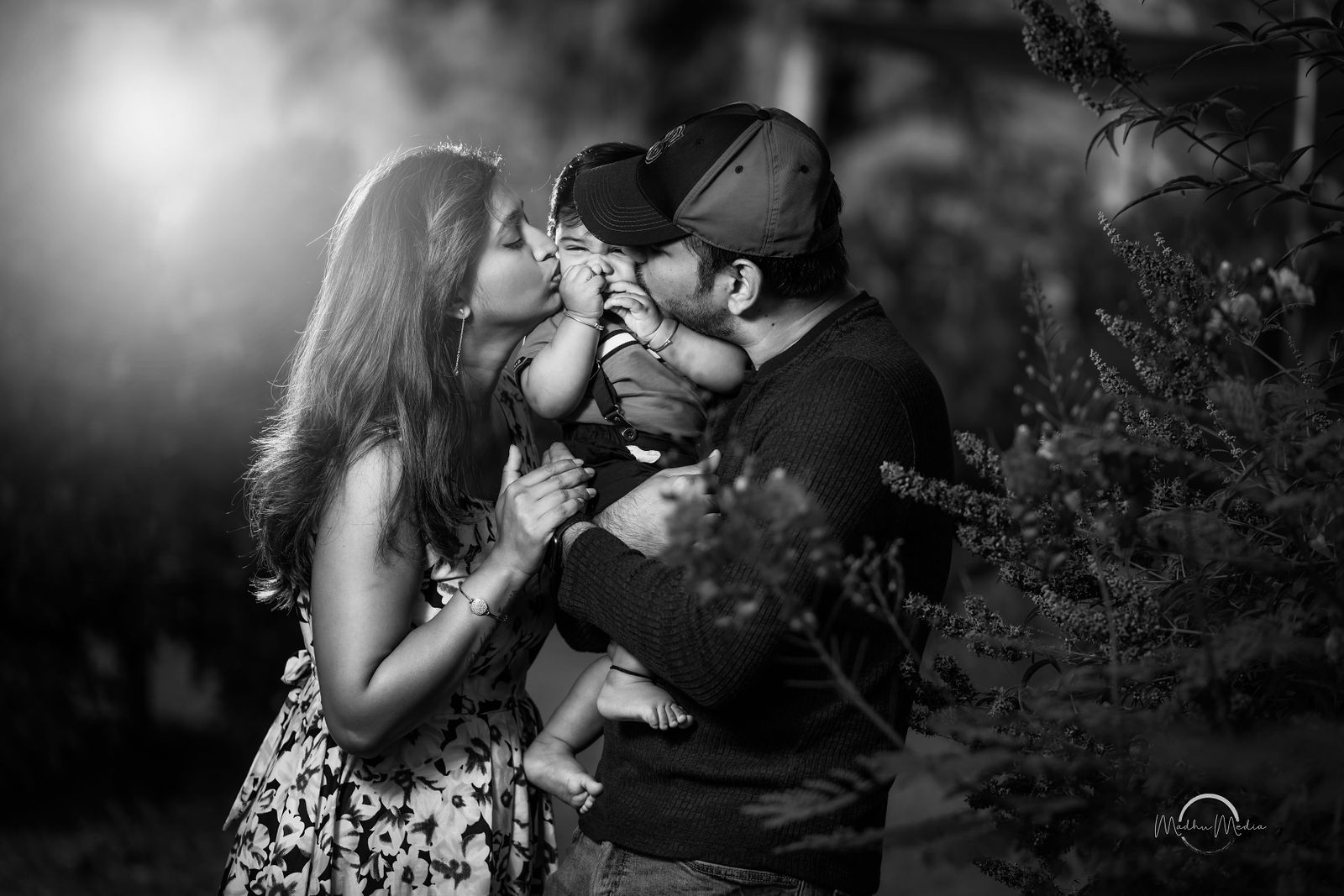 Parents kissing their baby, in black and white